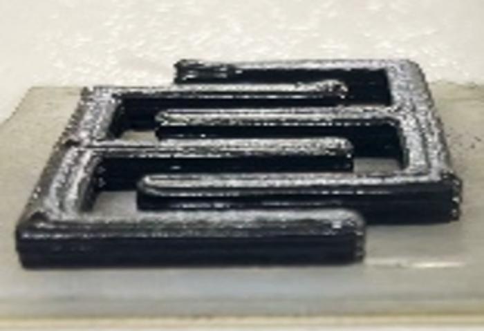 Black 3D-printed cement supercapacitor with two interlocking comb-shaped electrodes on a concrete slab