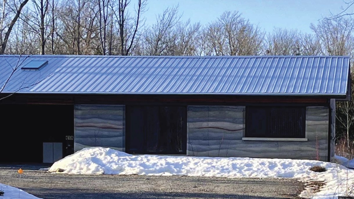 Single-storey rammed-earth guest house in southern Ontario in winter, with striped earth walls and snow along the base